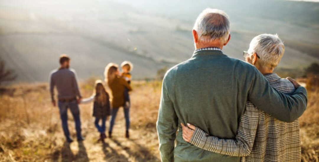 Back view of embraced grandparents enjoying while looking at their family on a field in autumn day.