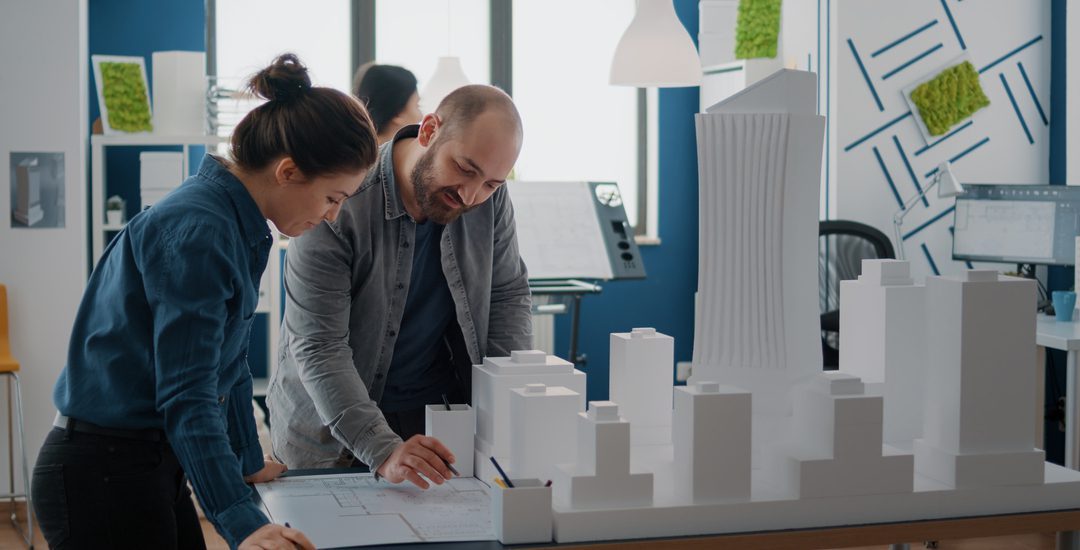 Team of colleagues using building model for inspiration to design construction layout. Man and woman working with maquette to plan blueprints and urban structure. Architectural project