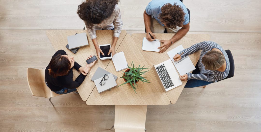 View from above. Business,startup, teamwork concept. Startup partners sitting at coworking space talking about future project, looking through examples of work on laptop and digital tablet