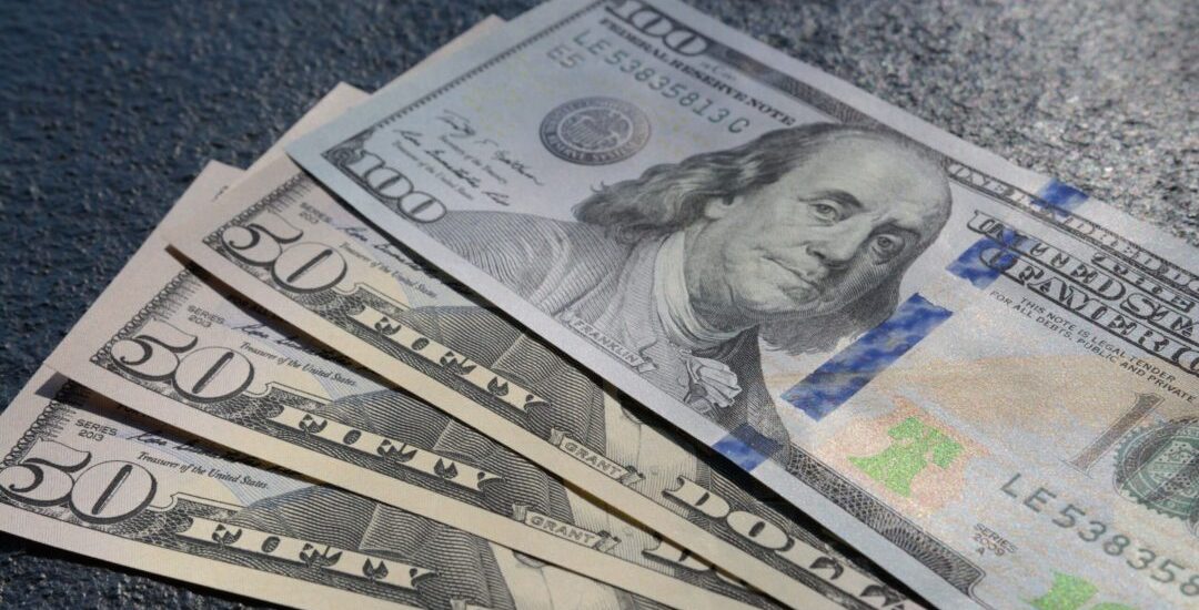 A closeup shot of three fifty and one hundred dollars bills on a gray background