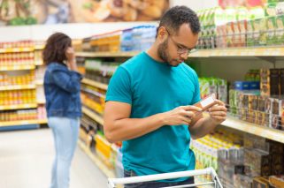 Focused African American man reading information on packaging. Concentrated bearded guy buying food at supermarket. Shopping concept