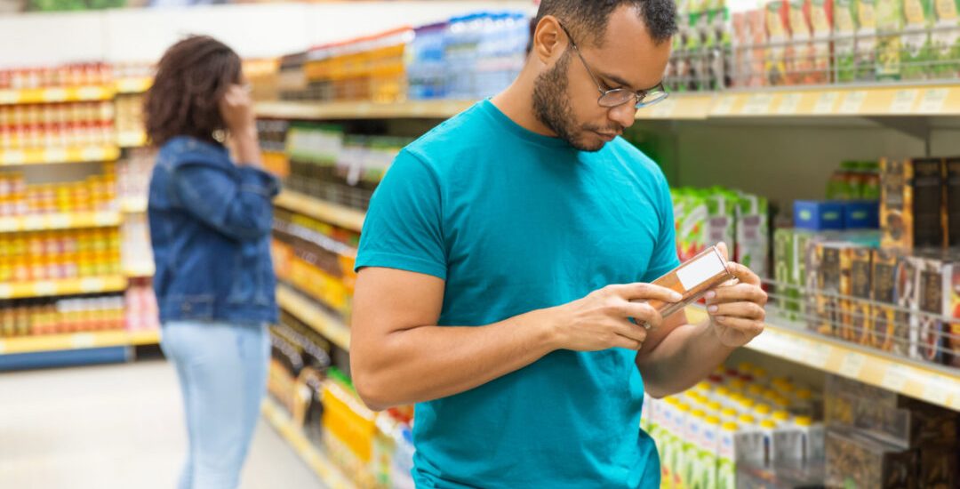 Focused African American man reading information on packaging. Concentrated bearded guy buying food at supermarket. Shopping concept