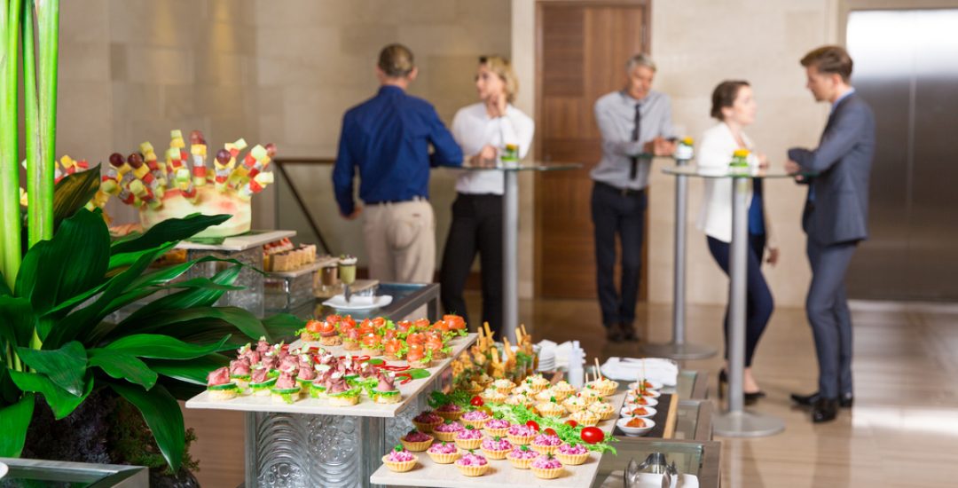 View of different canapes, tartlets and snacks on buffet table in restaurant. Business people eating and talking in background. Catering concept