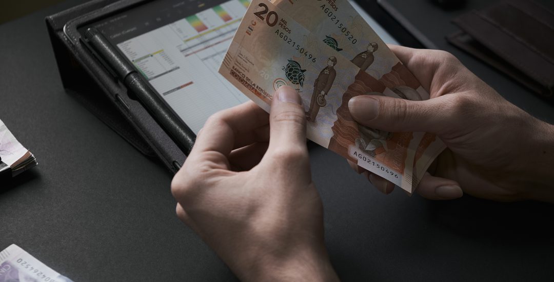 Male hands count colombian pesos banknotes in a dark office