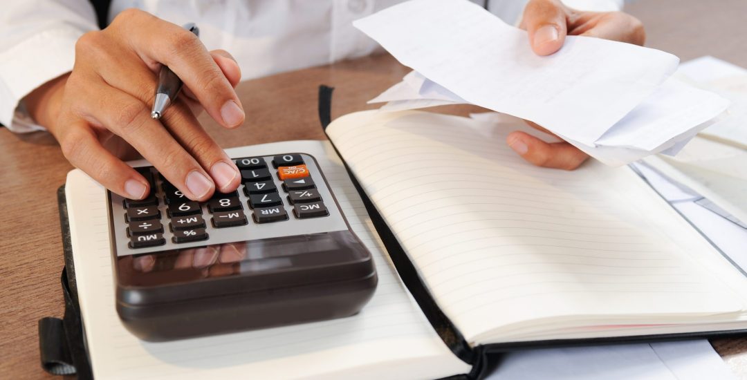 Closeup of person calculating bills on calculator. Notebook and calculator lying on desk. Accountancy concept. Cropped view.