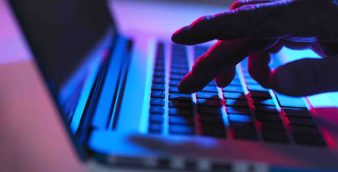 Silhouette of male hand typing on laptop keyboard at night