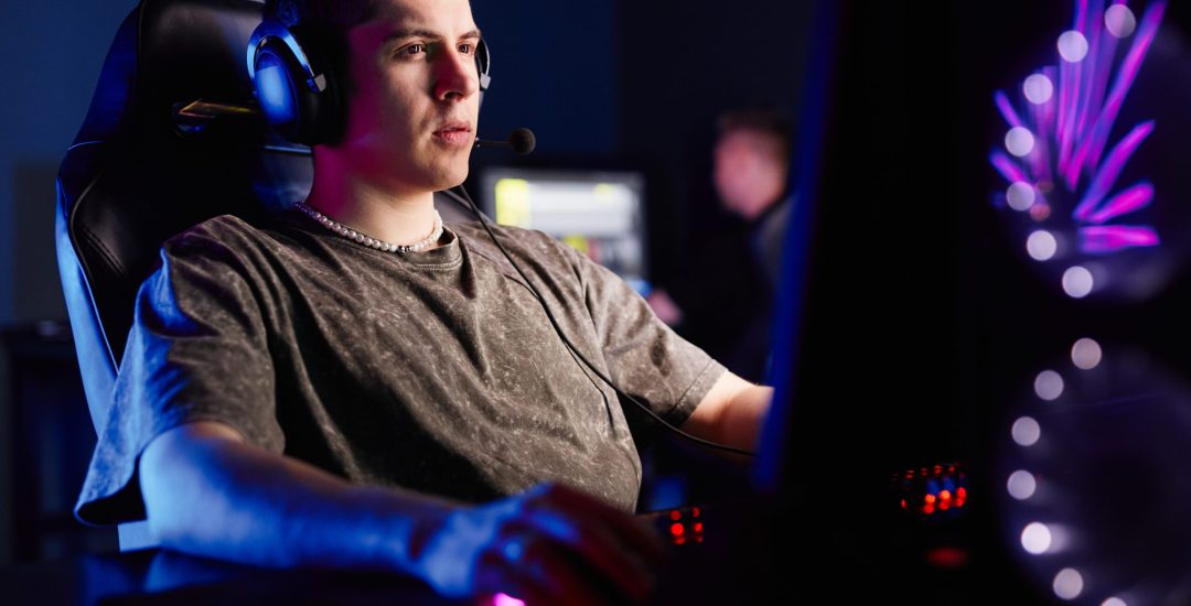 Side view portrait of Caucasian young man playing video games in dark with neon accent lights