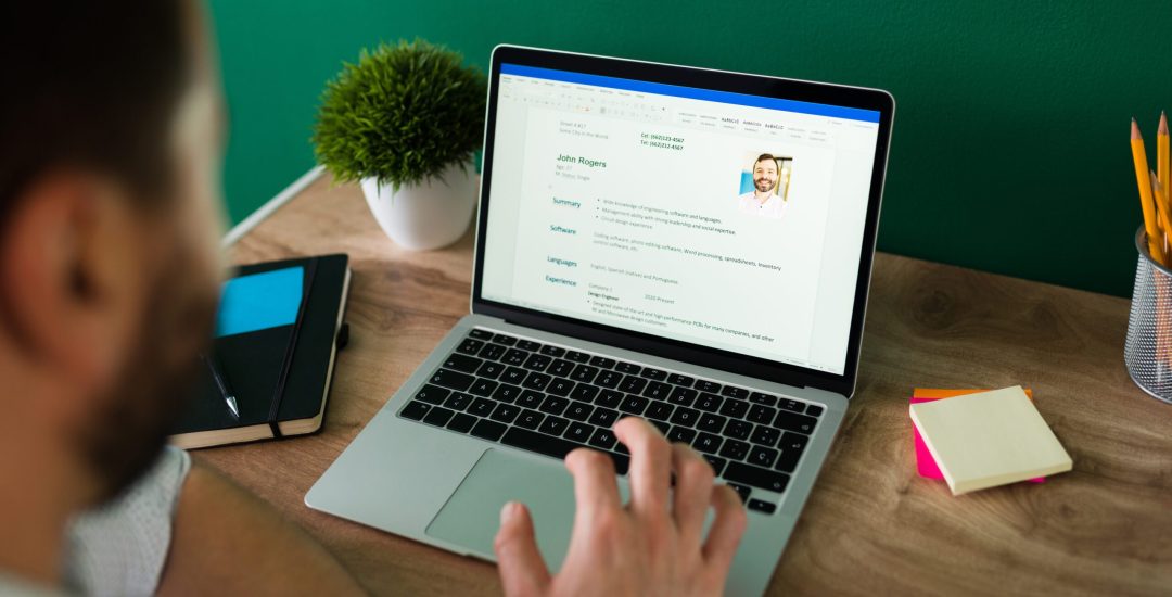 Rear view of an adult man searching for a new job and working on writing his resume on the laptop