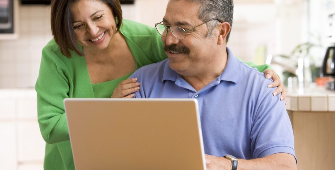 Couple in kitchen with laptop smiling