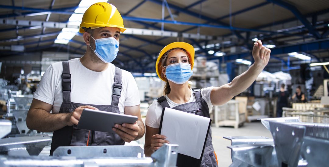 Factory workers with face masks protected against corona virus doing quality control of production in factory.