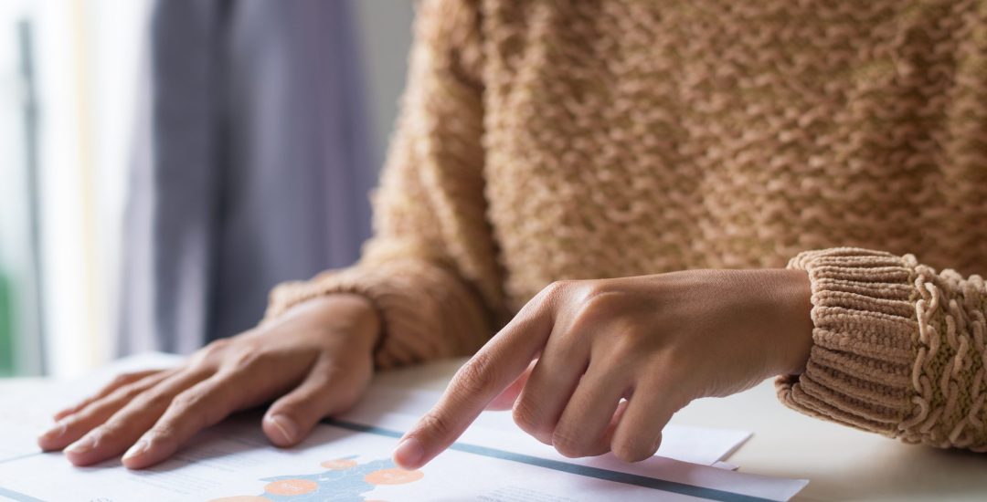 Close-up of busy analyst viewing data of social survey. Unrecognizable lady sitting at table and working with report. Examining data concept