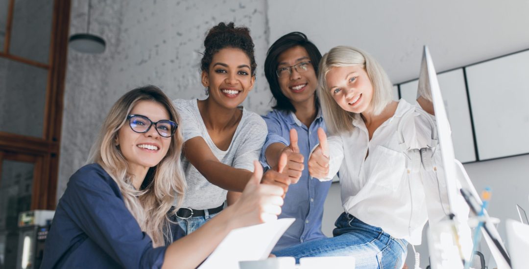 Blissful african female head of marketing department posing with thumb up after hard work. Indoor portrait of team of international business company enjoying good day.