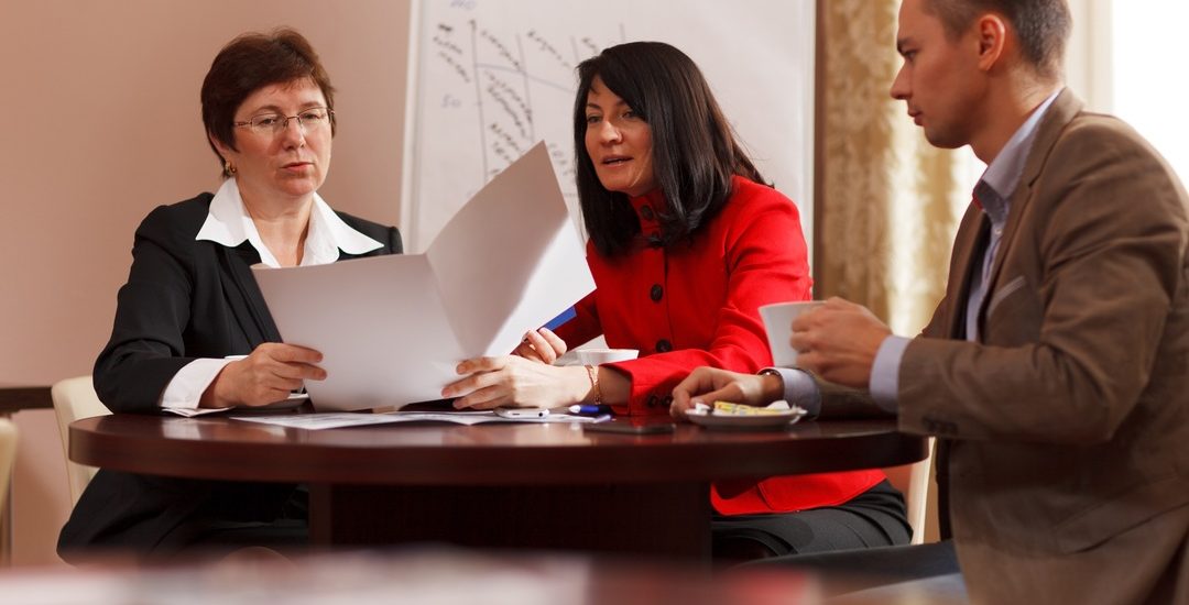 Businesspeople having a meeting over coffee sitting together at a table discussing a document, young man and two middle-aged women present