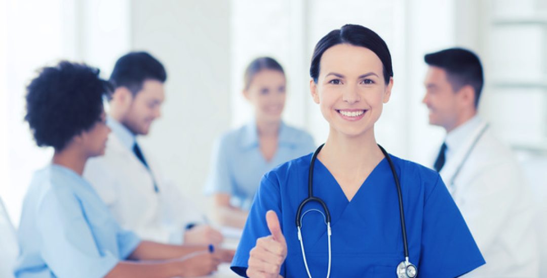 clinic, profession, people and medicine concept - happy female doctor over group of medics meeting at hospital showing thumbs up gesture