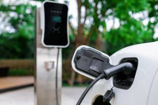 Focus closeup electric vehicle plugged in with EV charger device from blurred background of public charging station powered by renewable clean energy for progressive eco-friendly car concept.