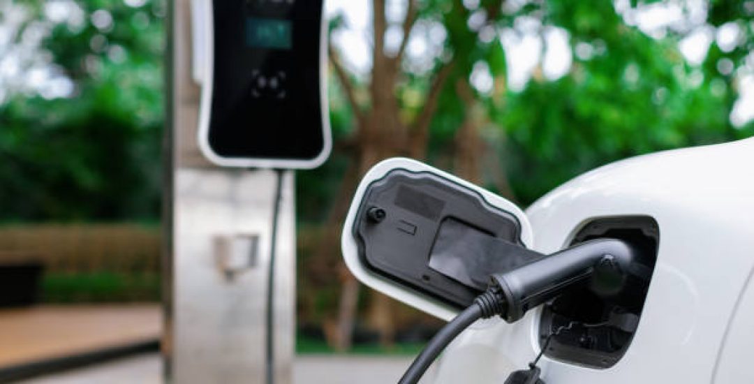 Focus closeup electric vehicle plugged in with EV charger device from blurred background of public charging station powered by renewable clean energy for progressive eco-friendly car concept.