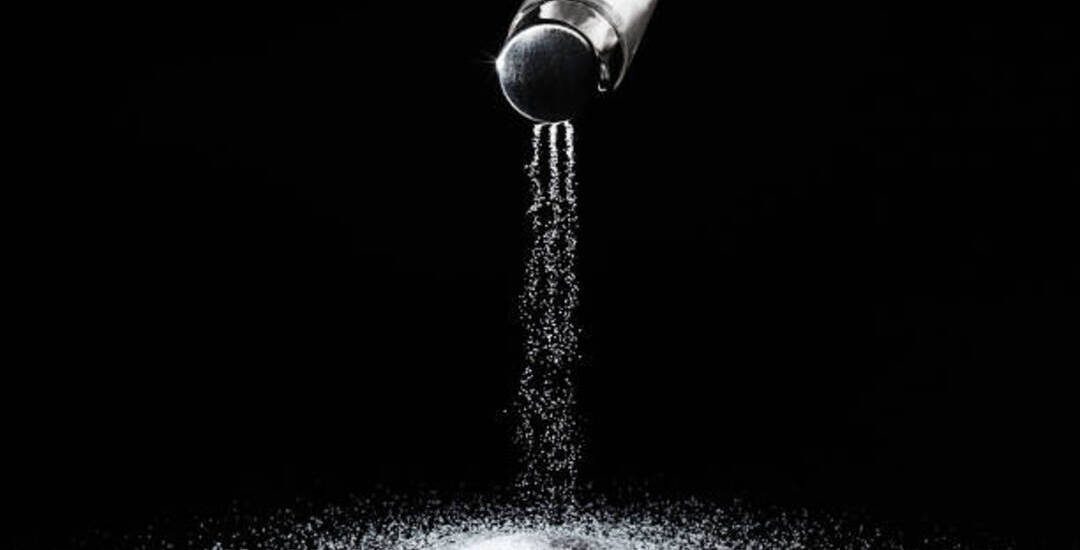 Salt spills out of the salt shaker in thin streams on a black background.Concept salting/