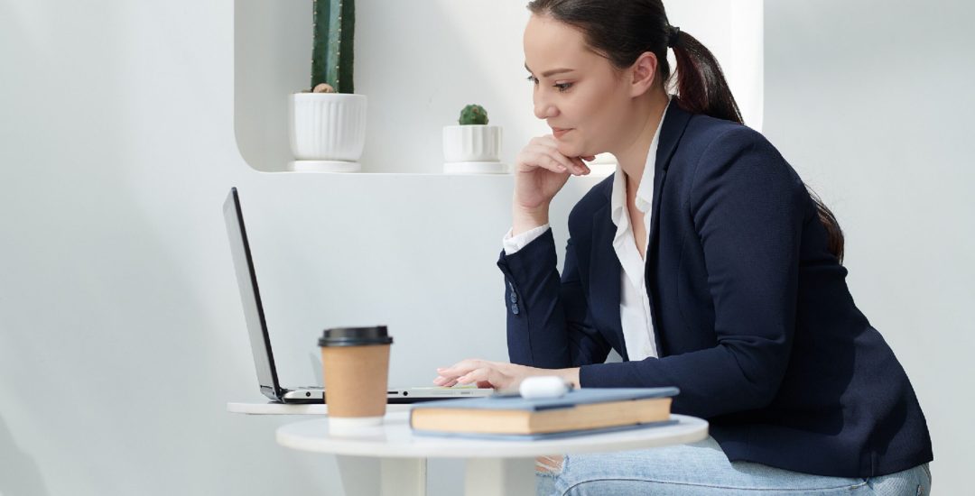 Pretty female university student working on laptop in cafe, writing article or essay