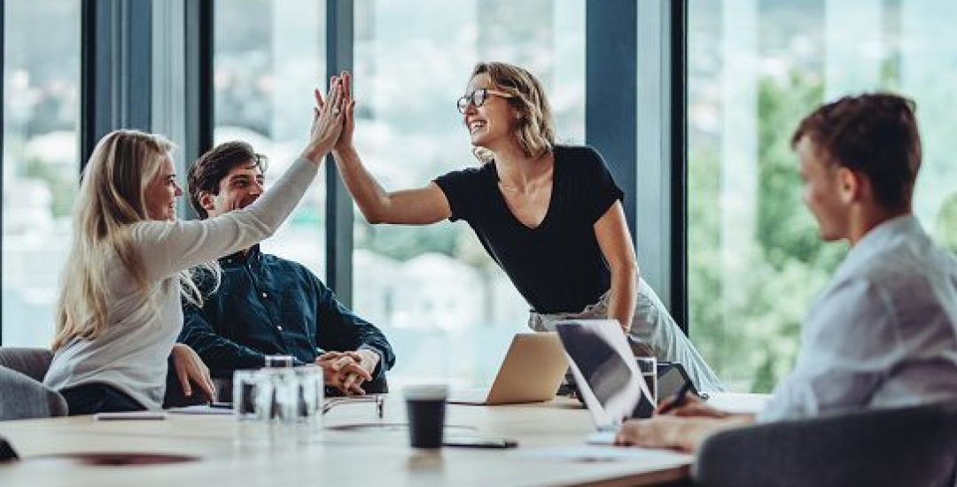 Female professional giving a high five to her colleague in conference room. Group of colleagues celebrating success in a meeting.