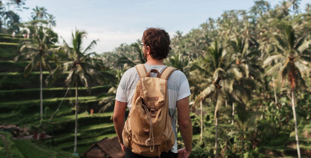 Back view of man explorer  with travel backpack enjoying natural environment of green  rise  plantation during trip in Bali .Tourist with rucksack standing in asia wild valley during treck.