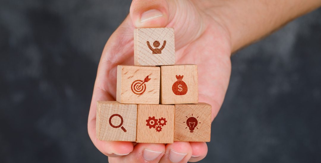 Business concept on grungy grey background side view. hand holding wooden blocks with icons.