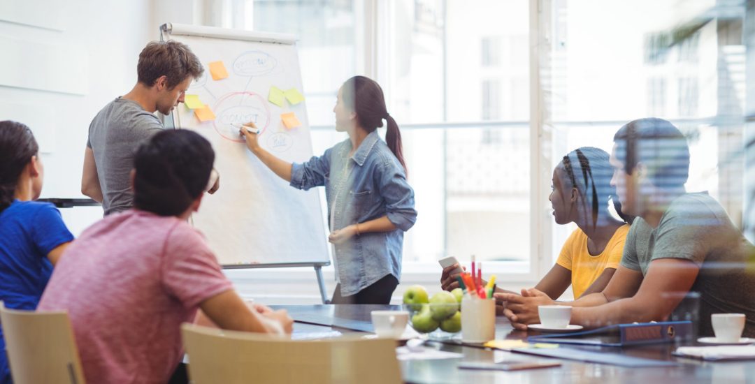 Business executives discussing with their colleagues on whiteboard during meeting at office