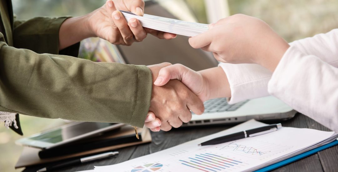 Business people shaking hands, finishing up meeting. businessman giving money to his partner while making contract - bribery and corruption concepts.