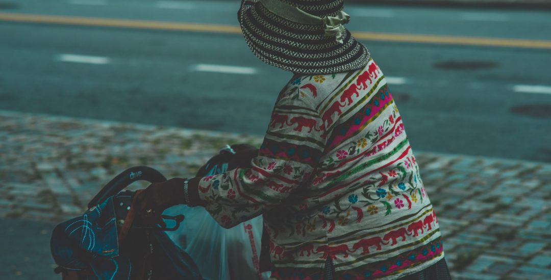 A closeup shot of an old female wearing a hat holding a stroller carriage