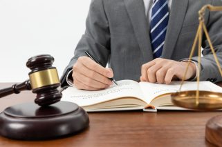 closeup-shot-person-writing-book-with-gavel-table