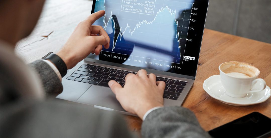 Cropped image of business man sitting by the table in cafe and analyzing indicators on laptop computer