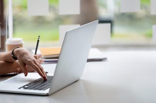 Cropped photo hand of woman writing making list taking notes in notepad working or learning online with laptop at home.