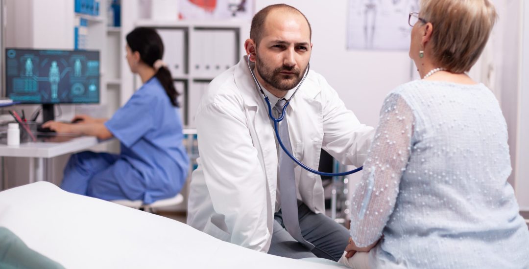 Doctor checking breathing problem of sick senior woman in hospital. Medical practitioner examining lungs of caucasian in modern clinic dressed in white coat.