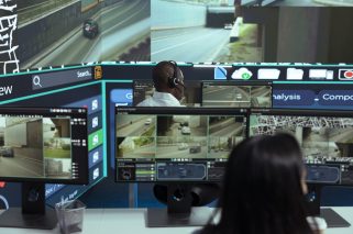 African american employee following delivery trucks around the city, sending gps coordinates for cargo location by using satellite map. Monitoring couriers in traffic on CCTV footage.