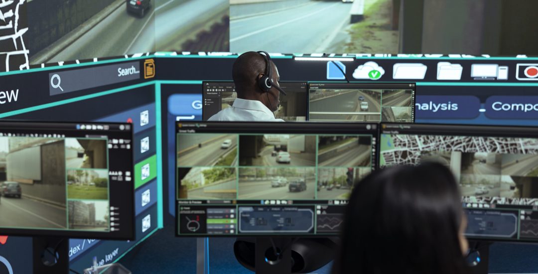 African american employee following delivery trucks around the city, sending gps coordinates for cargo location by using satellite map. Monitoring couriers in traffic on CCTV footage.