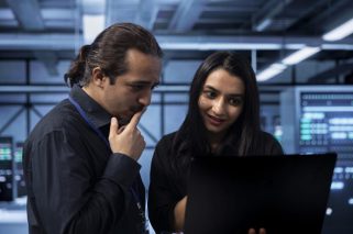 IT experts in server hub doing brainstorming, finding ways to ensure data remains shielded from potential threats. Employees chatting, safeguarding data center against unauthorized access using laptop