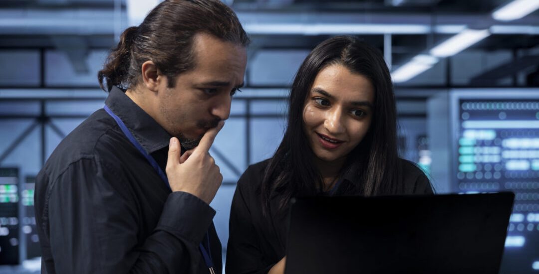IT experts in server hub doing brainstorming, finding ways to ensure data remains shielded from potential threats. Employees chatting, safeguarding data center against unauthorized access using laptop