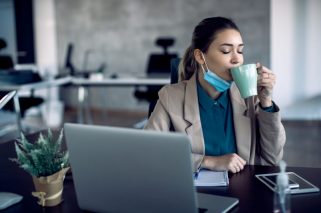 Young businesswoman drinking coffee with her eyes closed while working in the office during COVID-19 pandemic.