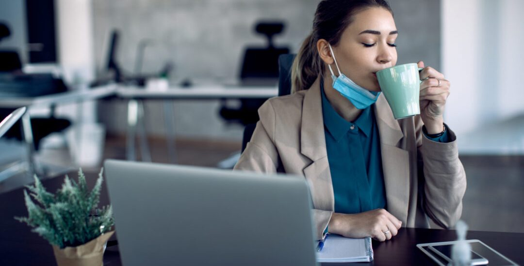 Young businesswoman drinking coffee with her eyes closed while working in the office during COVID-19 pandemic.