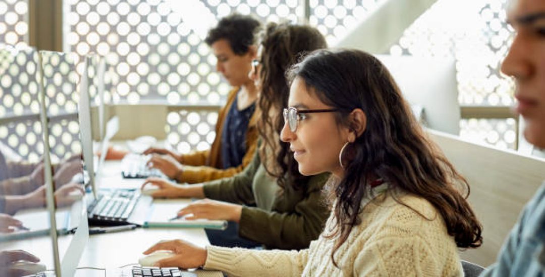 Young student studying in classroom. Female is looking at computer screen in university. She is in casuals.