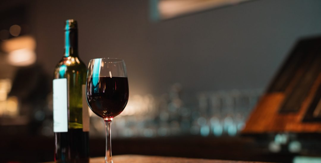 Glass of red wine and bottle on bar counter at bar