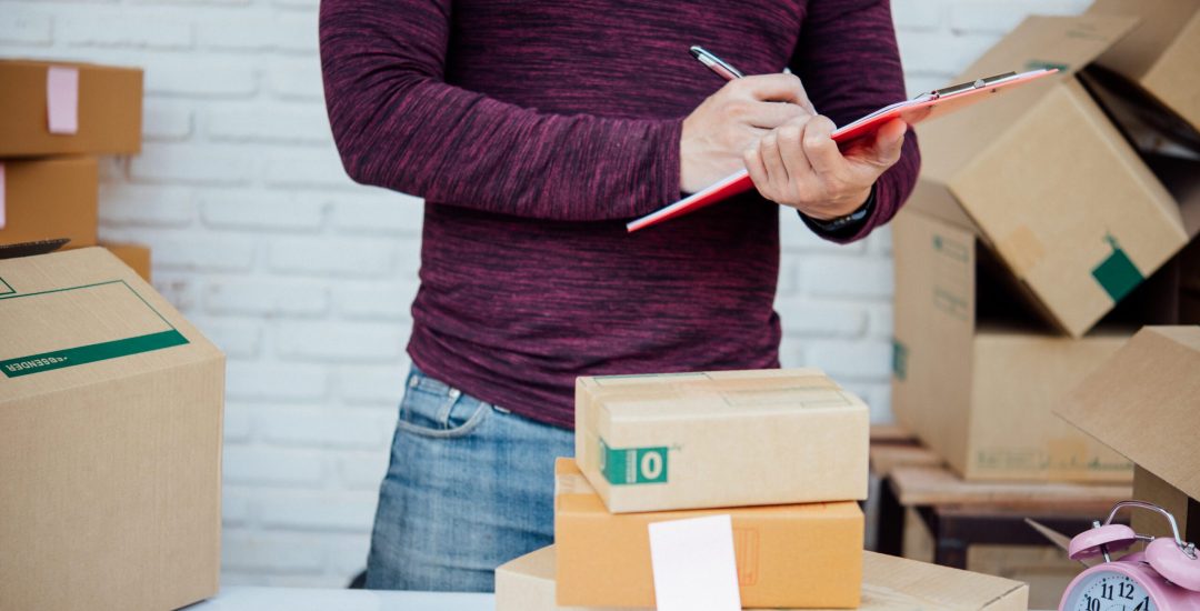 Handsome Young man working with papers among parcels at table in delivery department. online concept