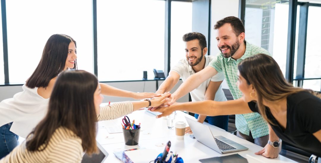 Happy business people celebrating success while stacking hands in motivational meeting at office