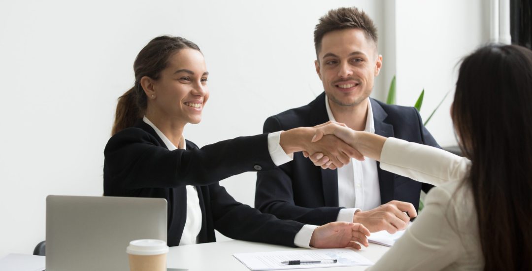 Smiling HR managers greeting female job applicant with handshake during recruiting or interview. Businesswoman making good first impression shaking hands of business partners. Partnership, cooperation