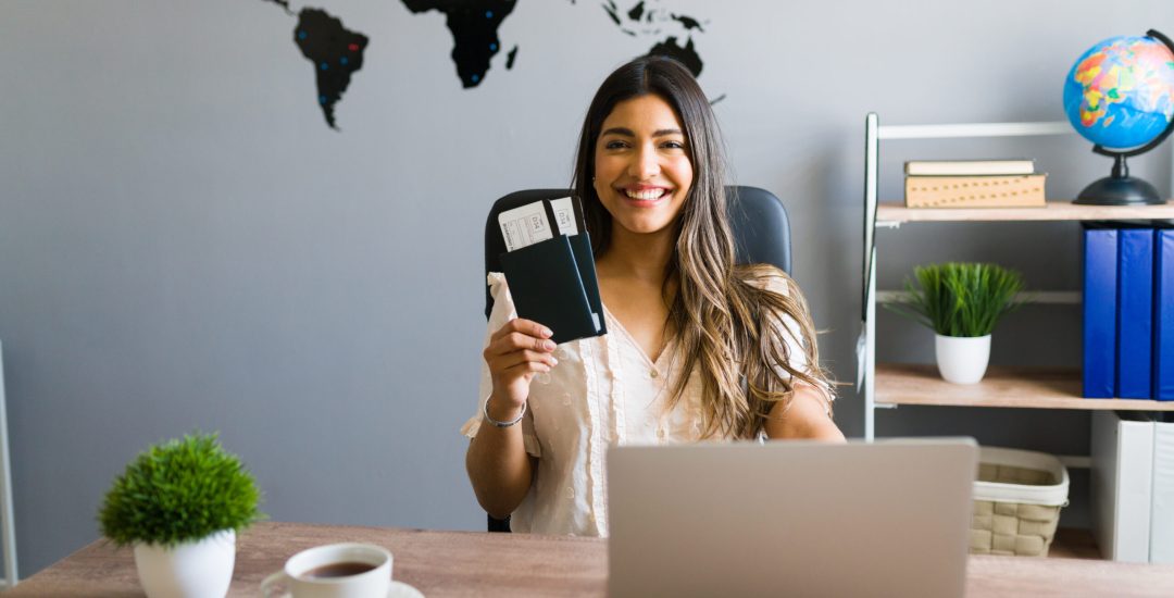 I am here to help you with your booking and travel questions. Female sales agent holding plane tickets while smiling and making eye contact at the travel agency