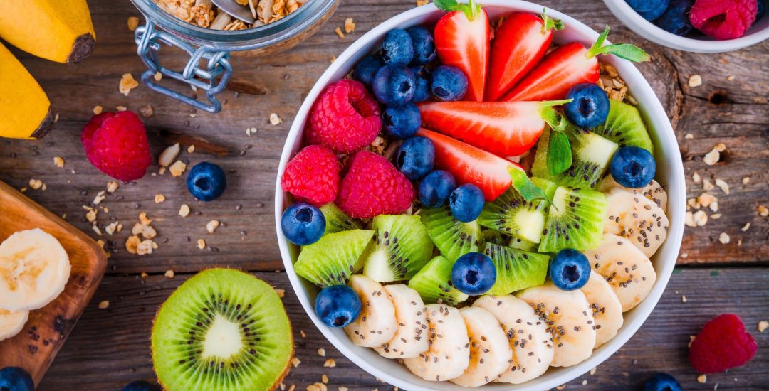 Breakfast bowl: granola with banana, kiwi, raspberry, strawberry, blueberry and chia seeds on wooden background