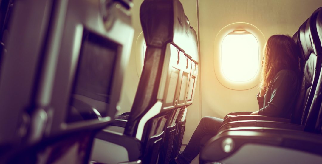 Lady is sitting in airplane looking out at shiny sun through window, vintage style photo