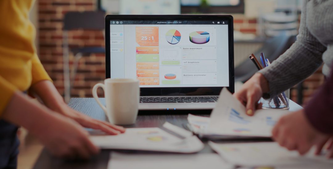 Laptop with financial diagrams and graphs on display in startup company office. Business people using documents with sales reports and analysis, working on partnership growth. Close up