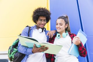 low-angle-view-teenage-couple-reading-book-standing-against-colored-wall