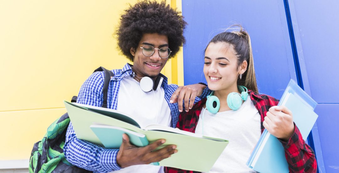 low-angle-view-teenage-couple-reading-book-standing-against-colored-wall