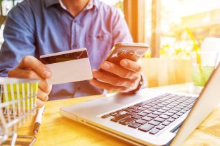 Man holding credit card in hand and entering security code using laptop keyboard.